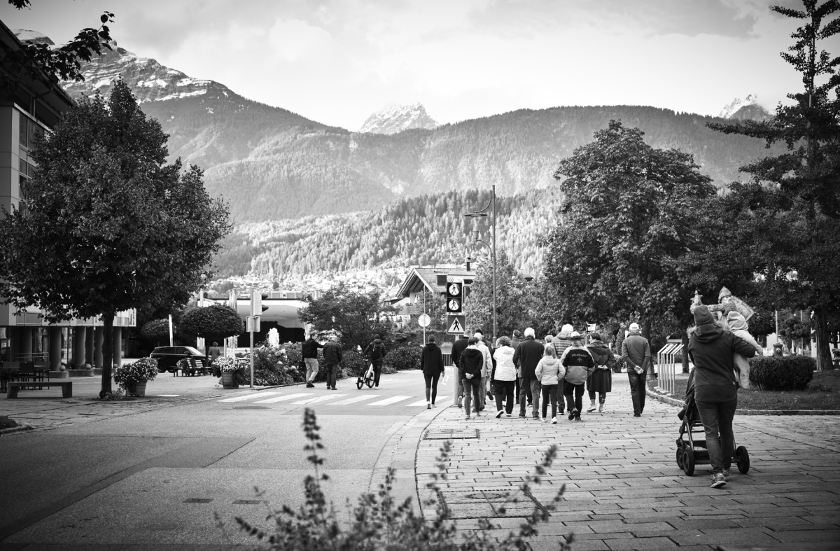Bild ist schwarzweiß und zeigt Personen spazieren auf den Straßen von Wattens vor Bergpanorama