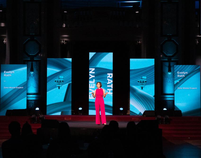Evelyn Rath in pinken Anzug auf der Bühne, im Hintergrund hochformatige Screen mit blauem Hintergrund und ihrem Namen.