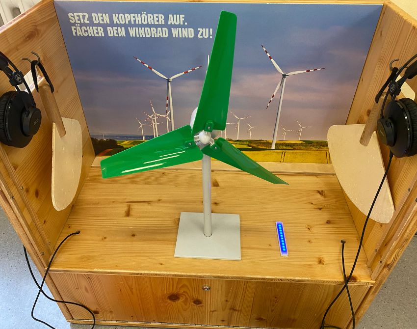 Windrad-Station der Klimaversum-Ausstellung mit Miniaturwindrad, Kopfhörern und Fächern